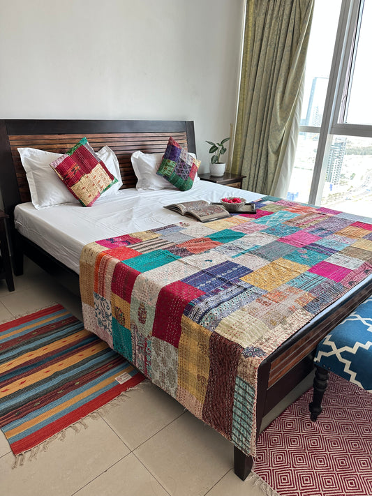 A colorful patchwork quilted kantha  bedspread is styled on bed for  a complete colorful boho style