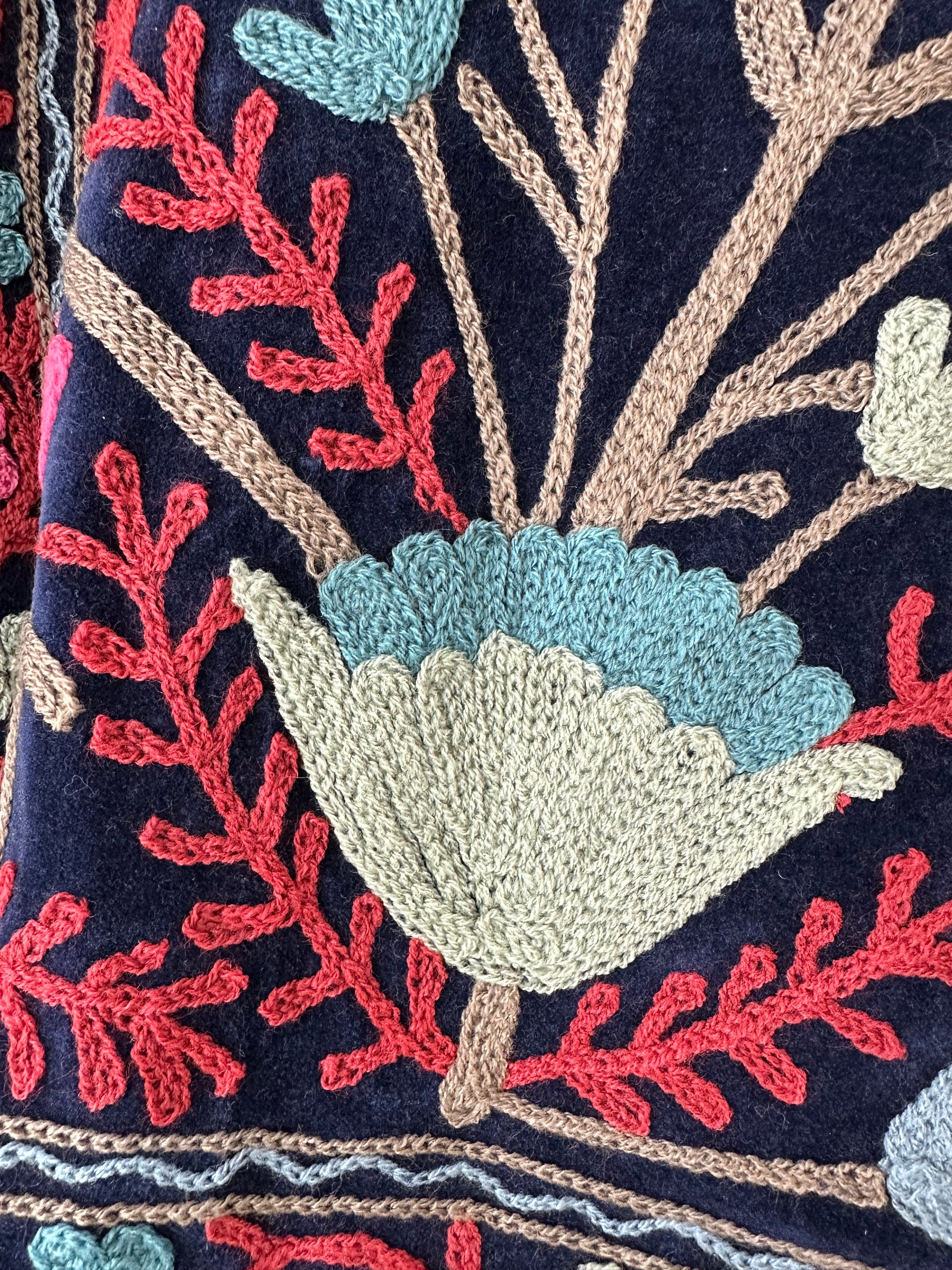 Colorful royal blue embroidered velvet jacket on a hanger against a white wall. Luxurious holiday outfit made by artisans in India for Ornate Handicrafts