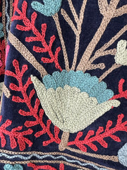 Colorful royal blue embroidered velvet jacket on a hanger against a white wall. Luxurious holiday outfit made by artisans in India for Ornate Handicrafts