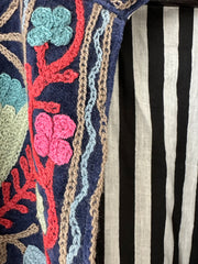 Colorful royal blue embroidered velvet jacket on a hanger against a white wall. Luxurious holiday outfit made by artisans in India for Ornate Handicrafts